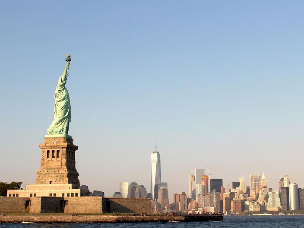 The image shows the Statue of Liberty with the New York City skyline in the background, including the One World Trade Center.